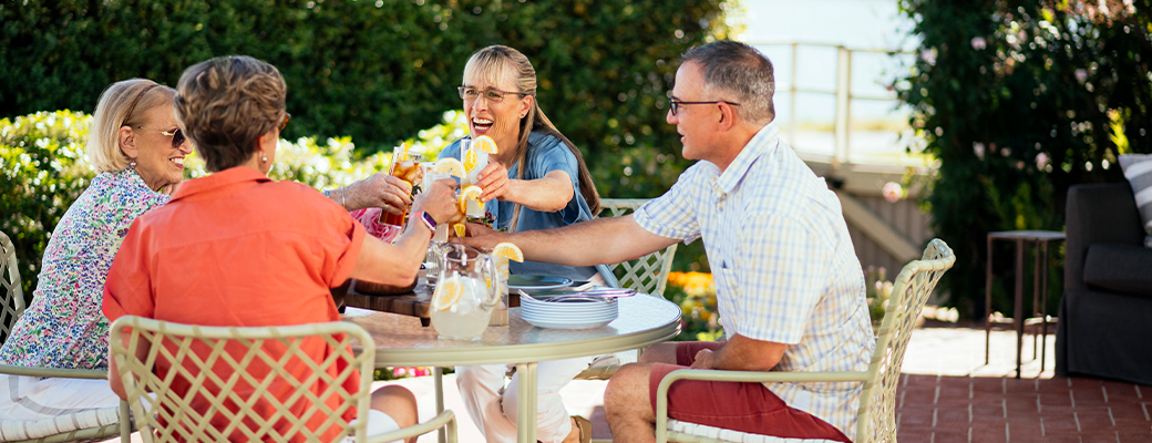 Image of three middle aged women and one middle aged man toasting over an outdoor patio meal